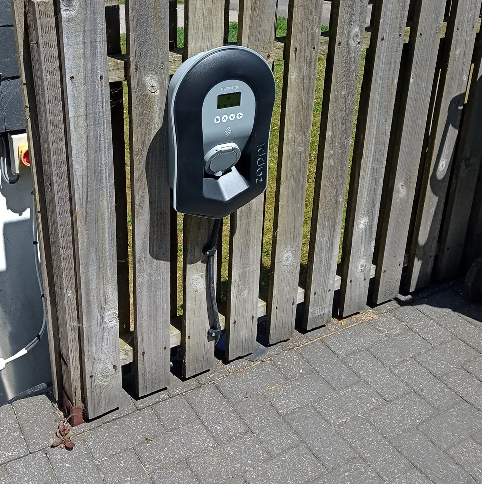 Zappi EV charger and its supply cable mounted on a timber fence in a private parking space